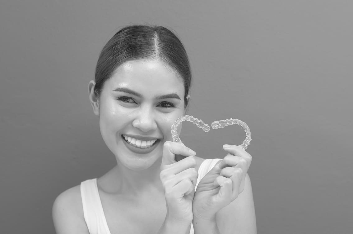 A young smiling woman holding invisalign braces